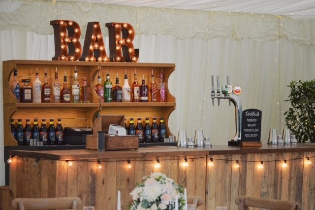 A marquee wedding reception with a rustic wooden mobile bar setup.